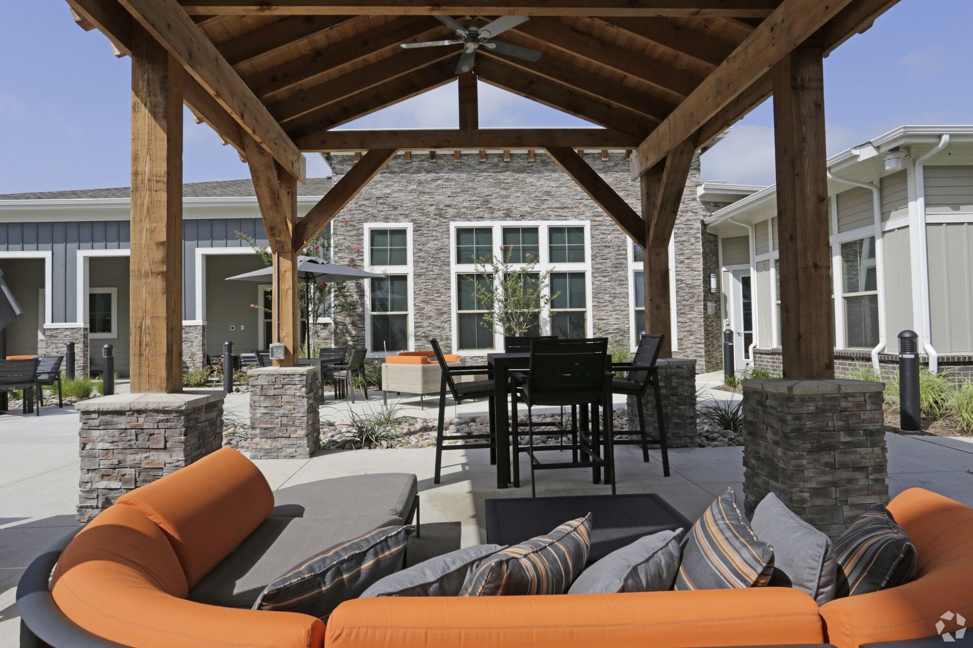 Outdoor community courtyard with a wooden pergola, lounge seating, and stone columns.