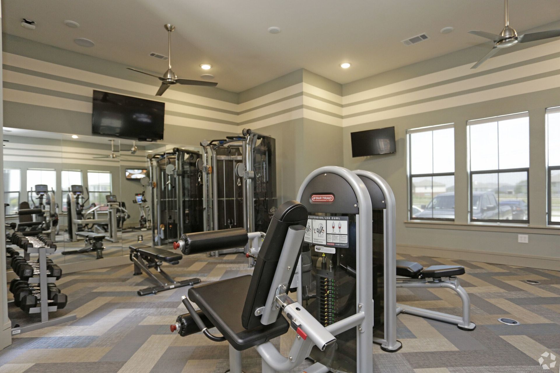 Indoor community fitness center with weight machines, benches, and cardio equipment.