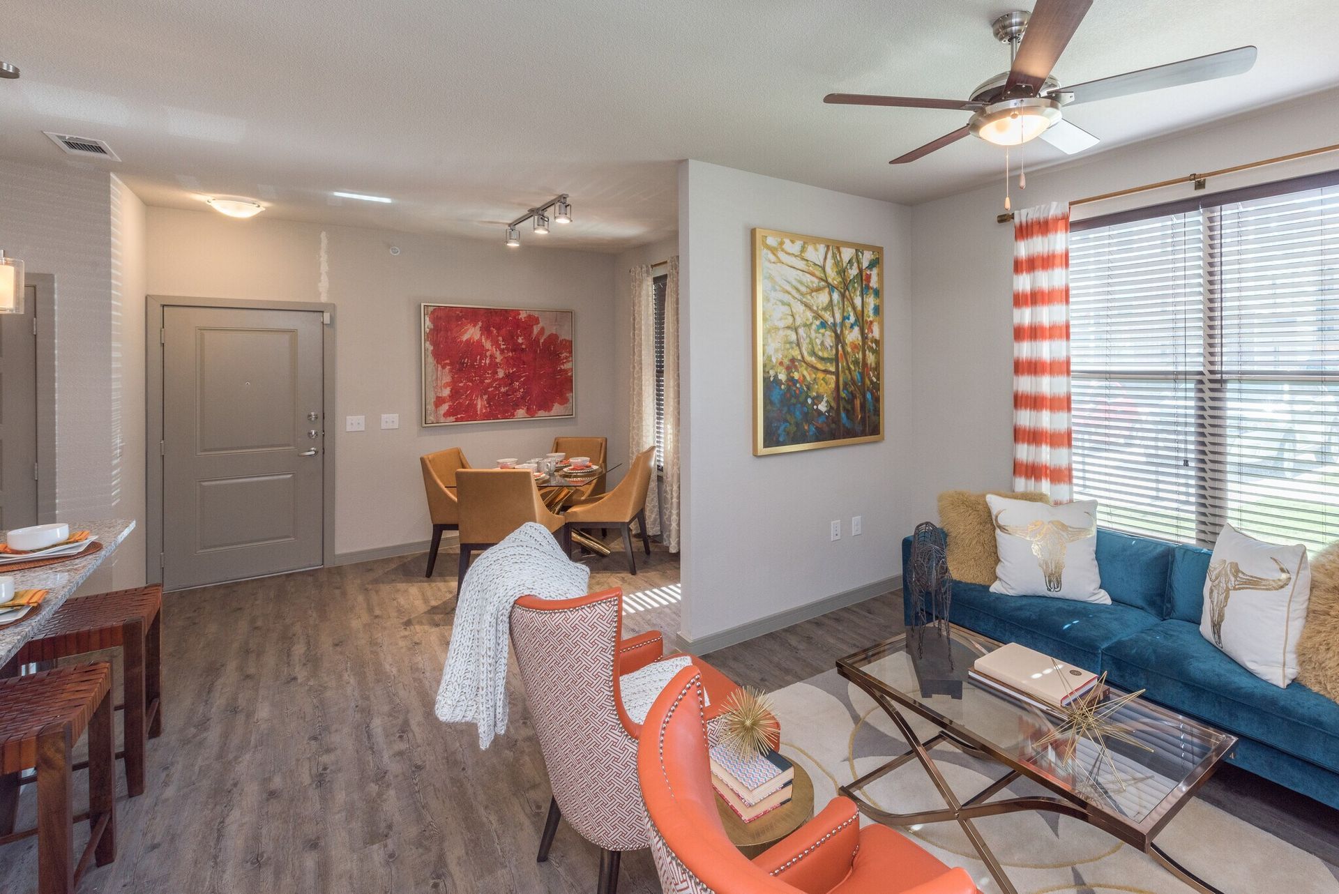 Open-concept living room and dining area with blue sofa, orange chairs, coffee table, and large window.
