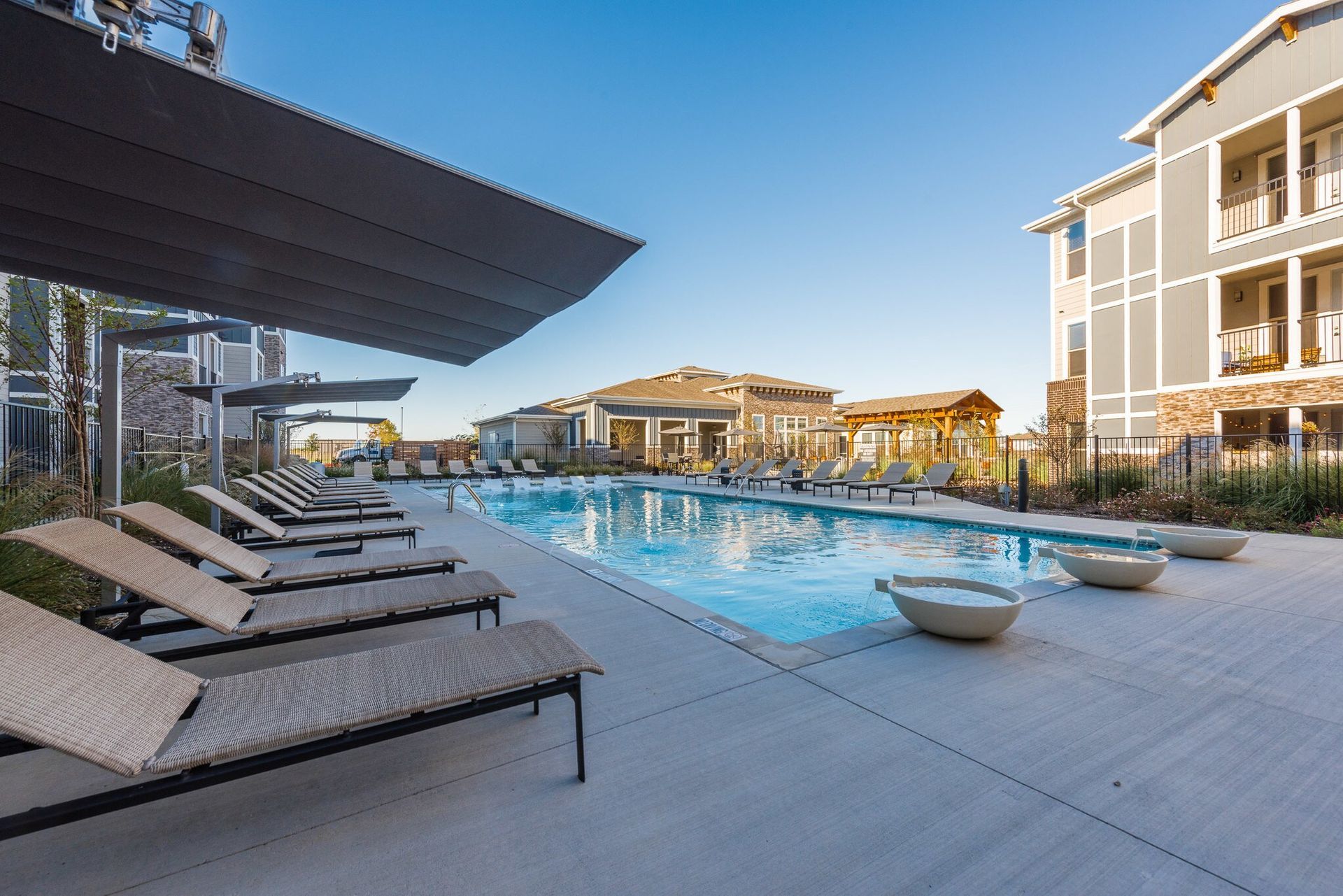 Outdoor apartment pool with lounge chairs and shade canopies