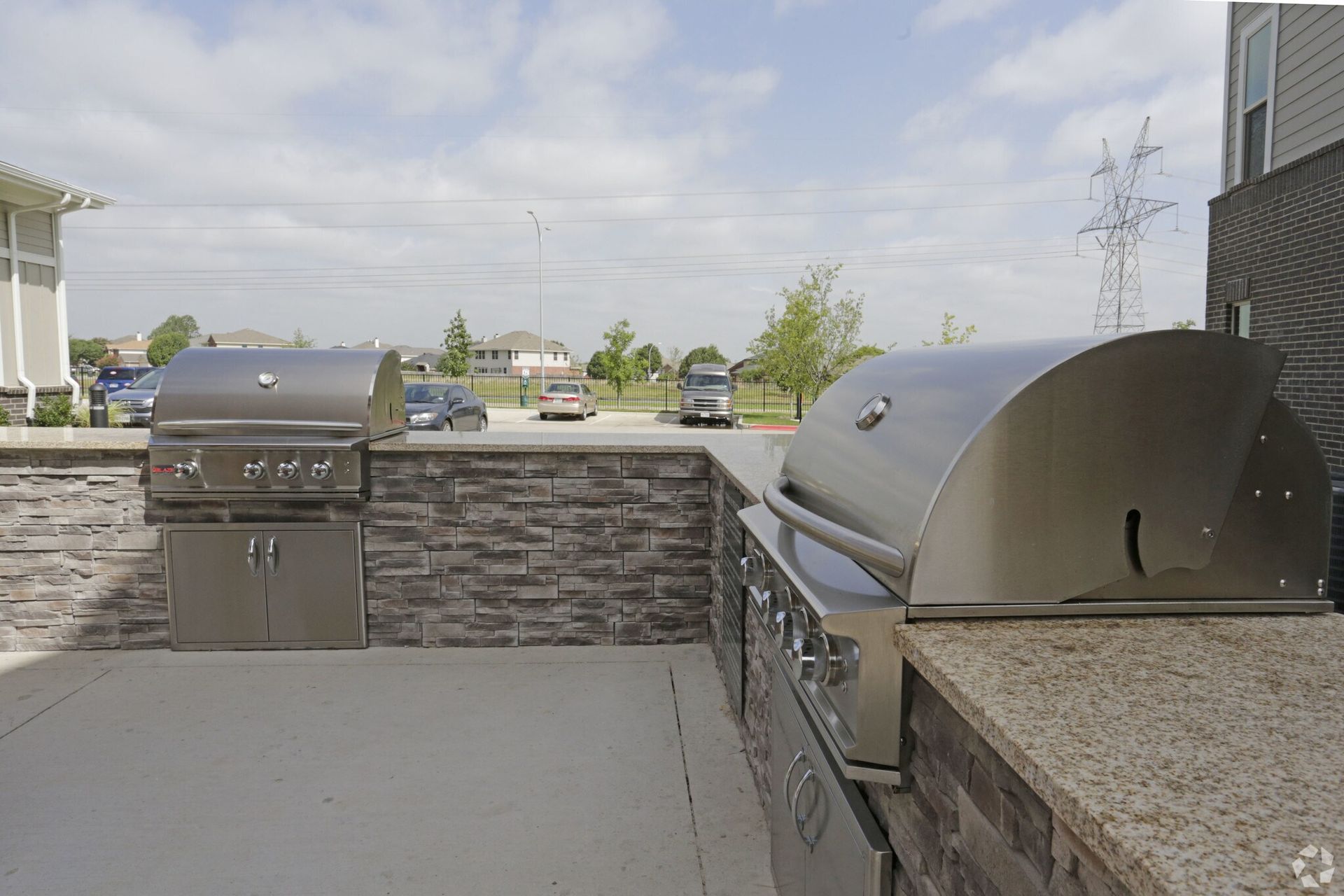 Outdoor communal grilling area with stainless steel grills and stone countertops.