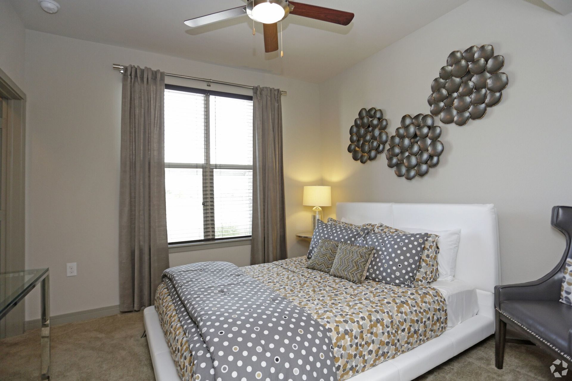 Bedroom featuring a white upholstered bed, gray polka-dot bedding, and circular metal wall art.