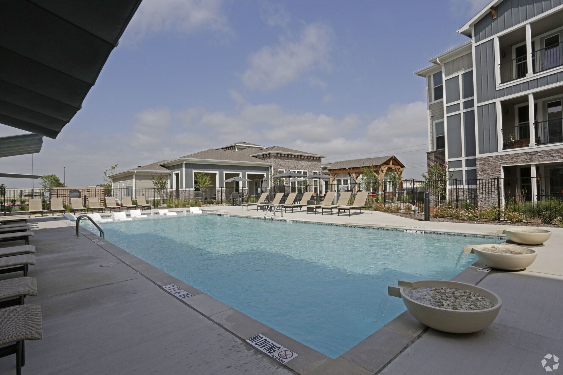 Outdoor pool area at an apartment community with lounge chairs and modern buildings in the background.
