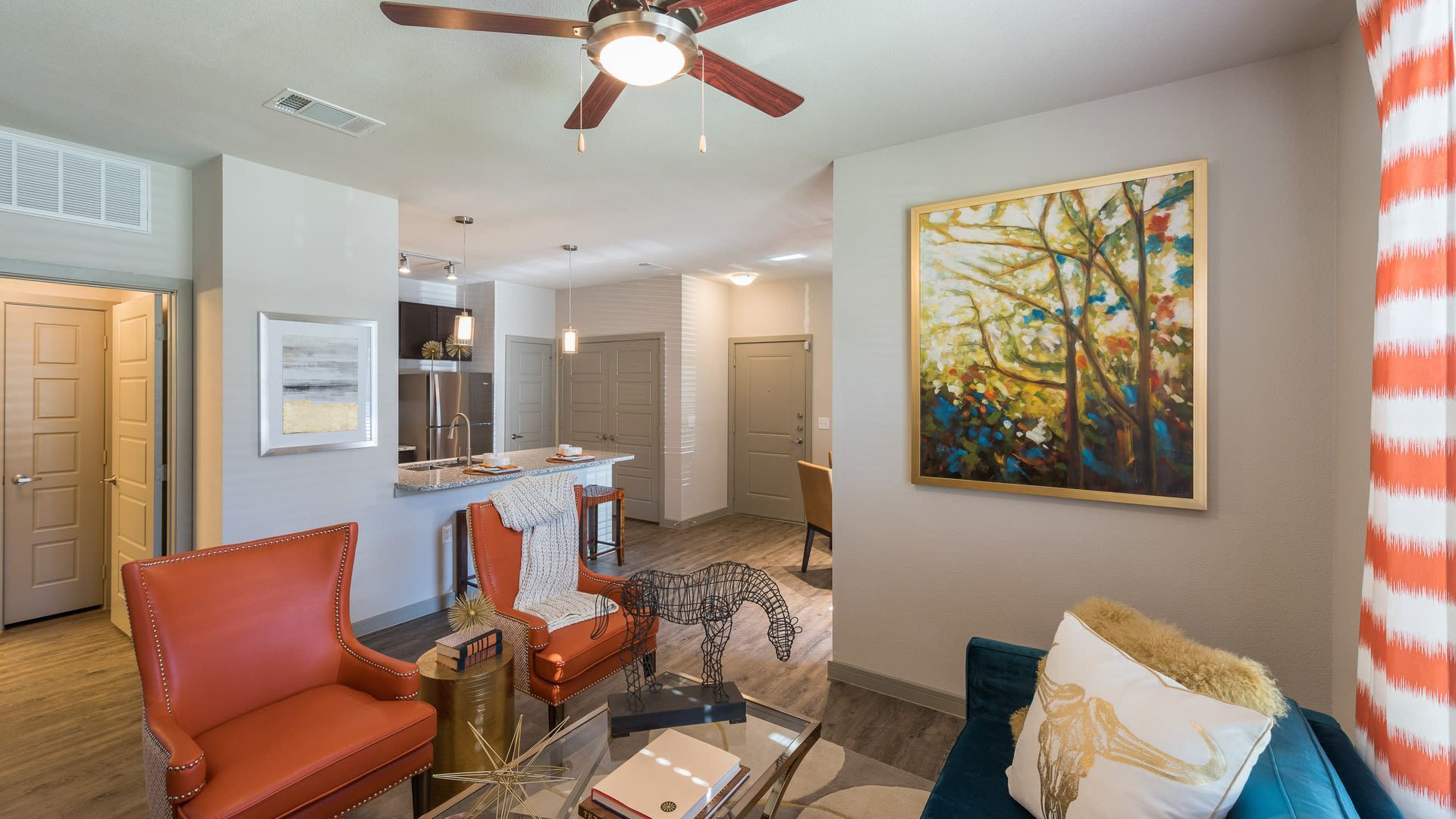 Open-concept living area with a kitchen island, orange chairs, and colorful wall art.