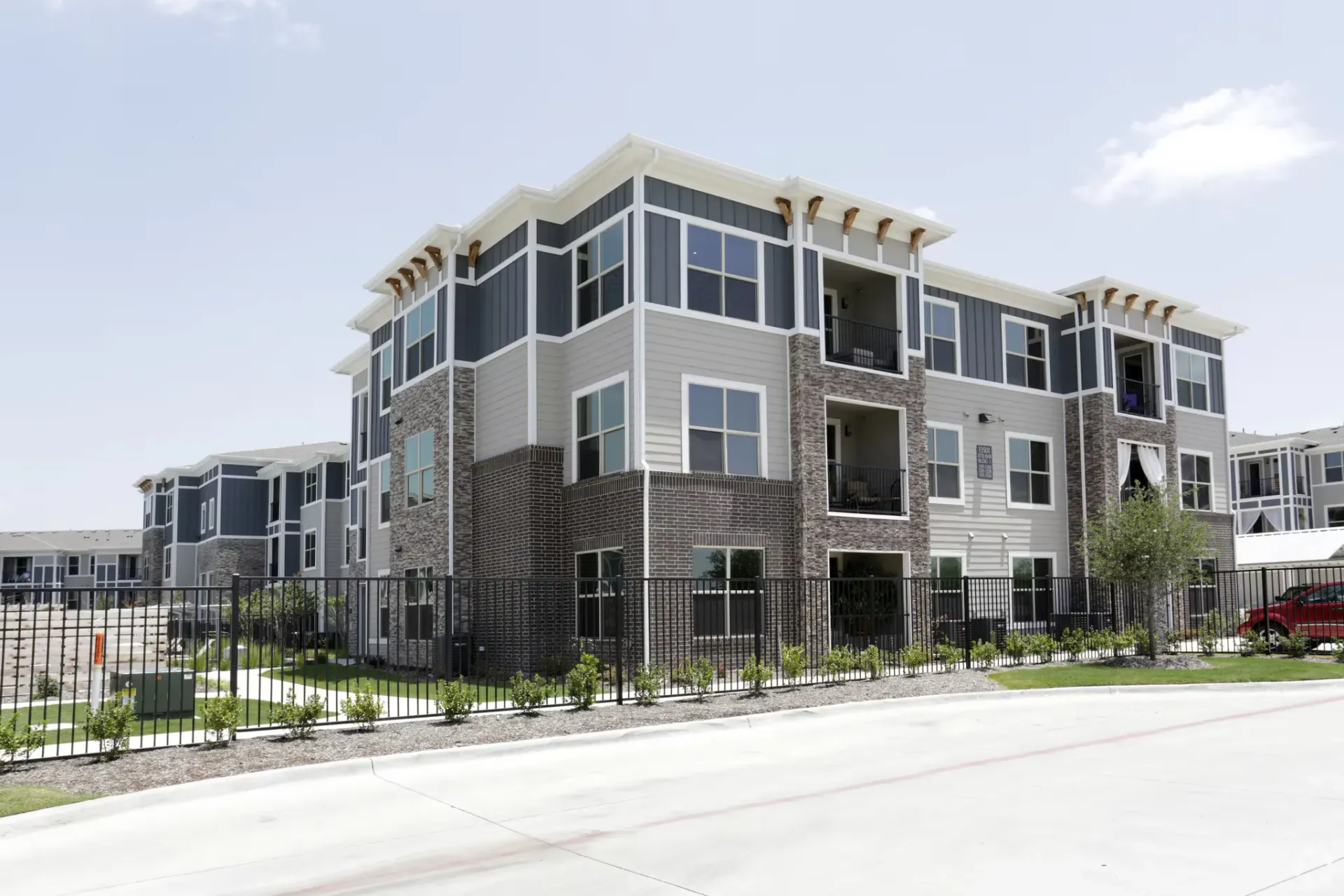 Exterior view of a modern, multi-story apartment building with brick first floor, gray siding, and balconies.