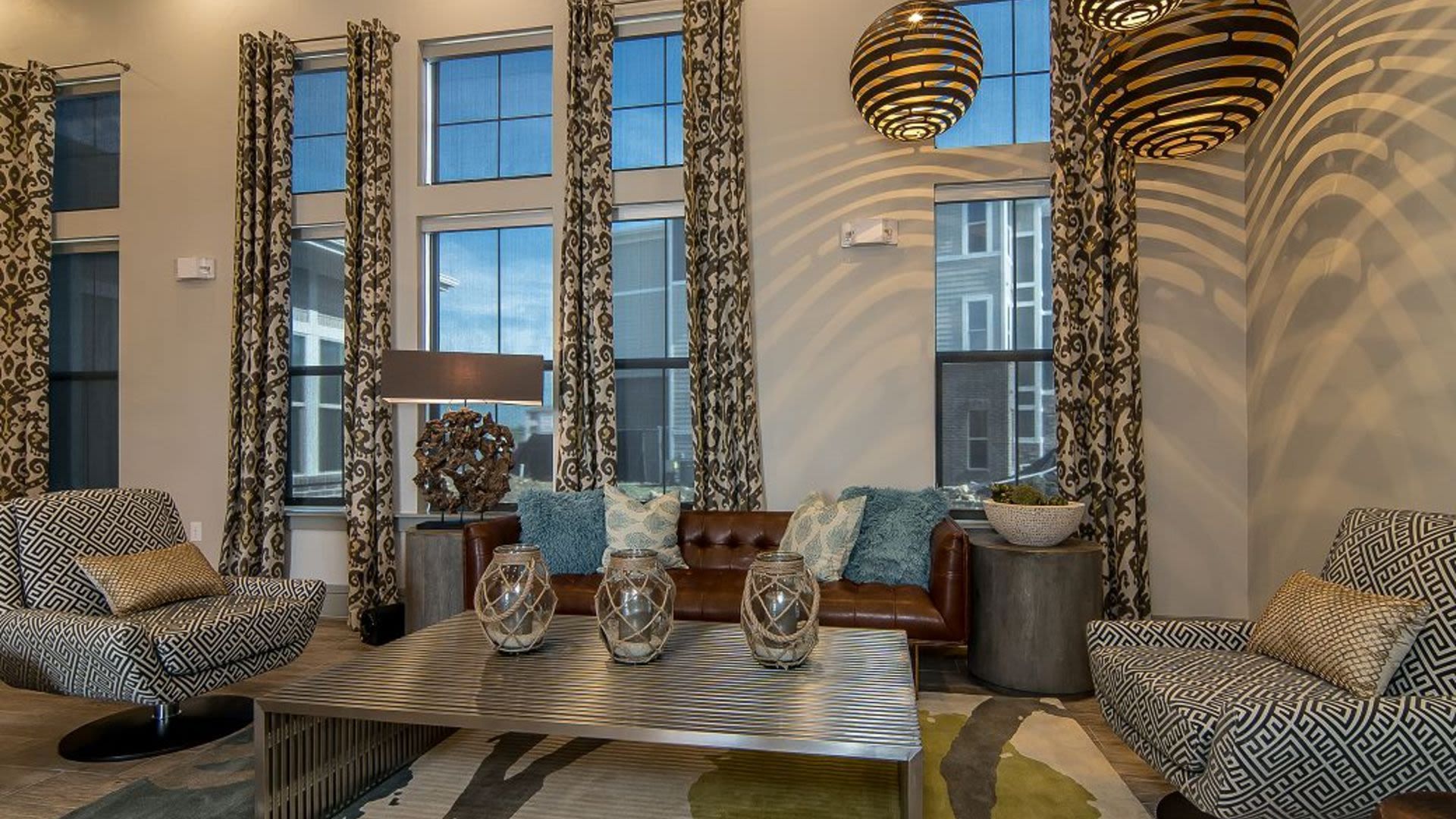 Modern community lounge with patterned chairs, a leather sofa, and large windows.