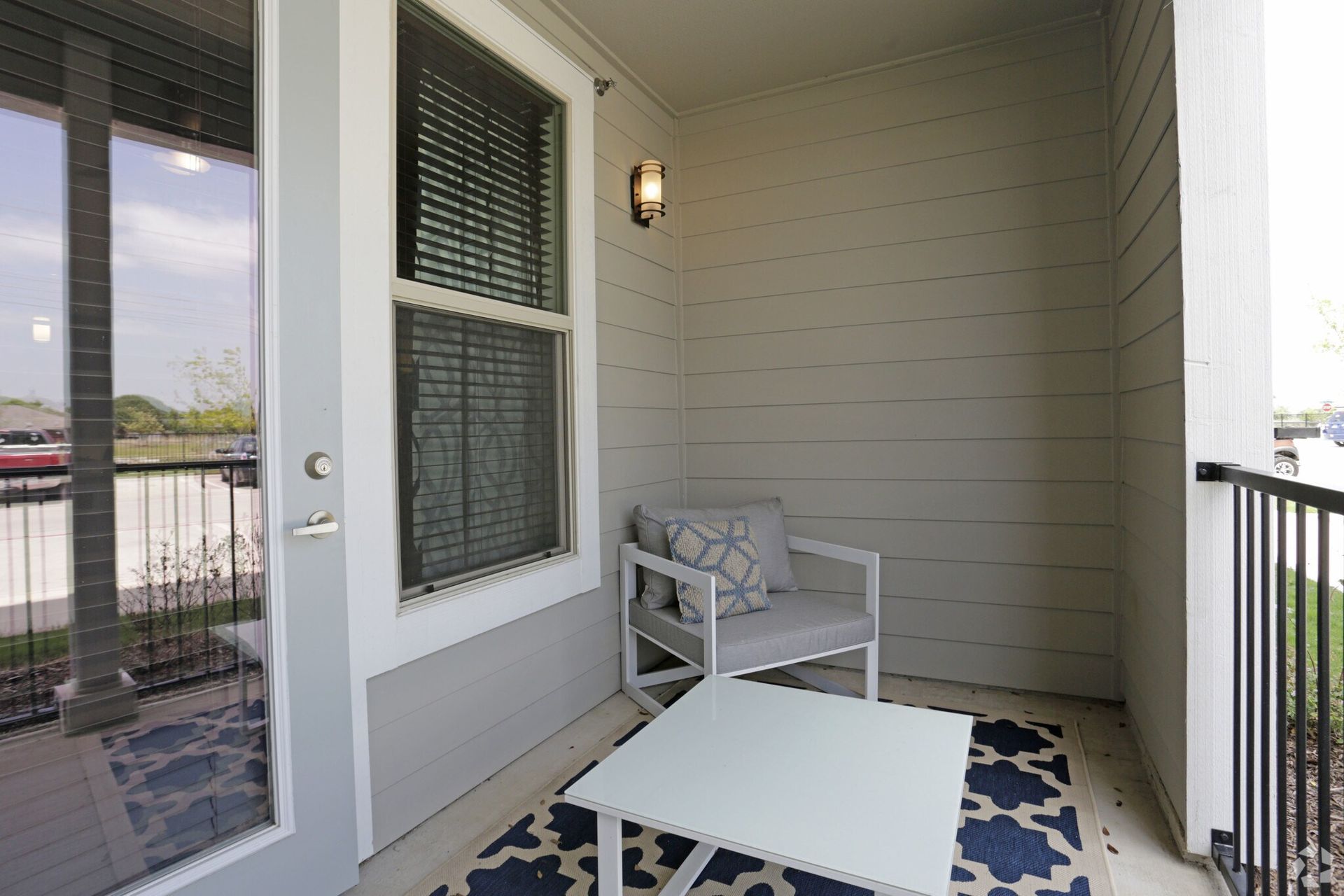 Private balcony with a white chair, cushions, a white coffee table, and a blue patterned rug.