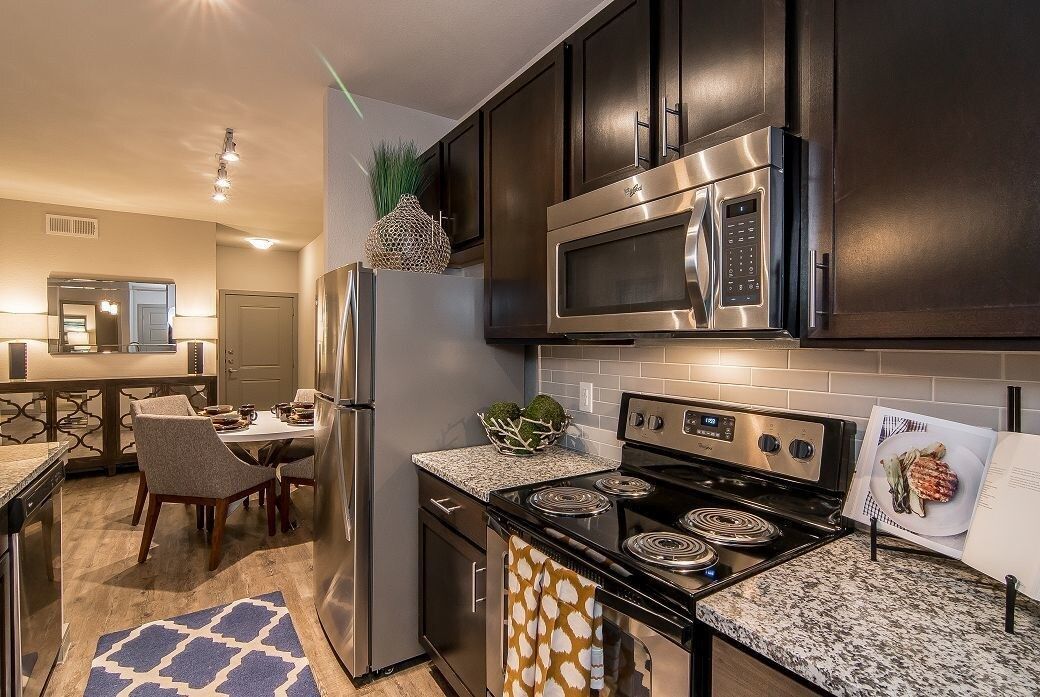 Modern kitchen in an apartment with dark cabinets, granite counters, and stainless steel appliances.
