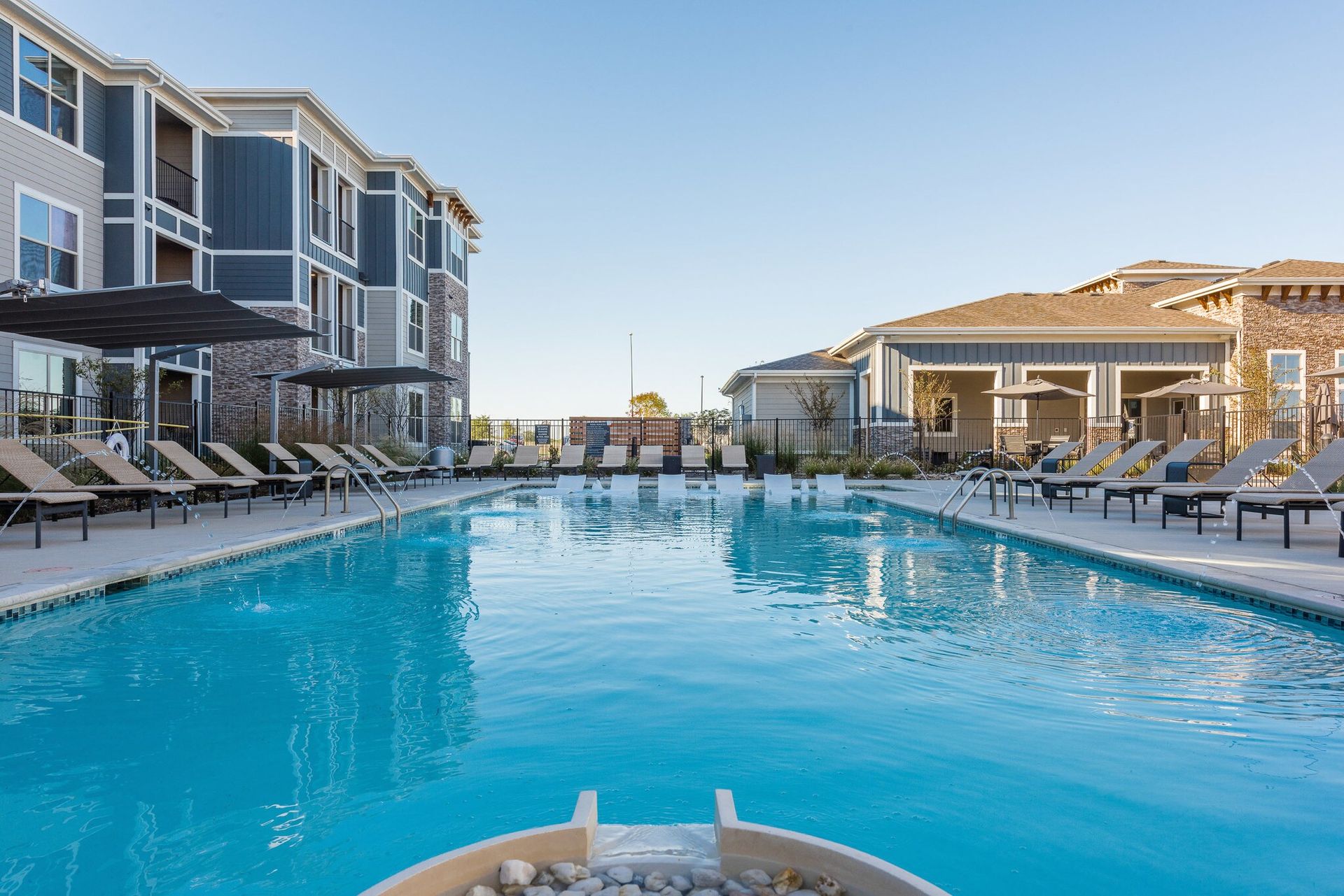 Outdoor community pool with lounge chairs beside apartment buildings.