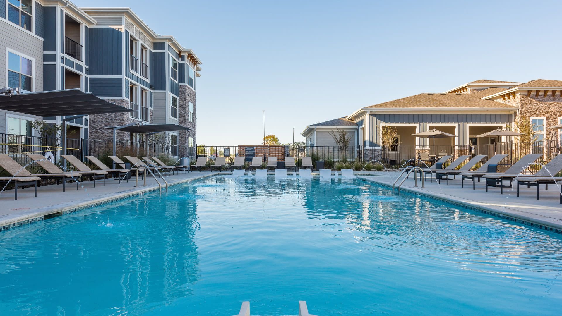 Outdoor pool area at an apartment community with lounge chairs and umbrellas.