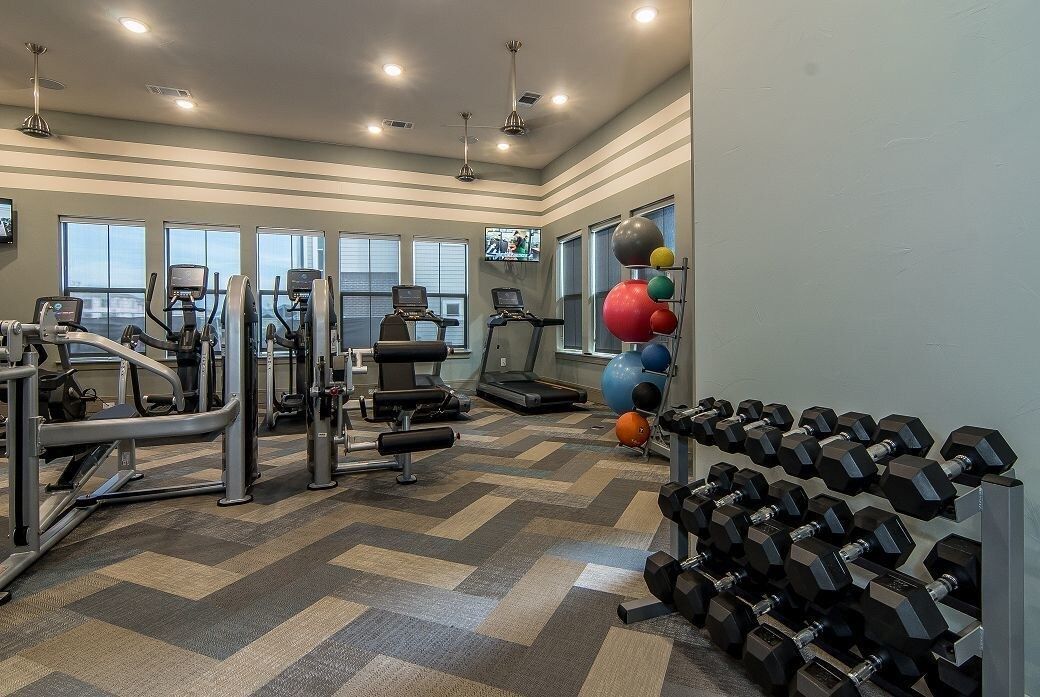 Interior of a communal fitness center with treadmills, weight machines, free weights, and medicine balls.