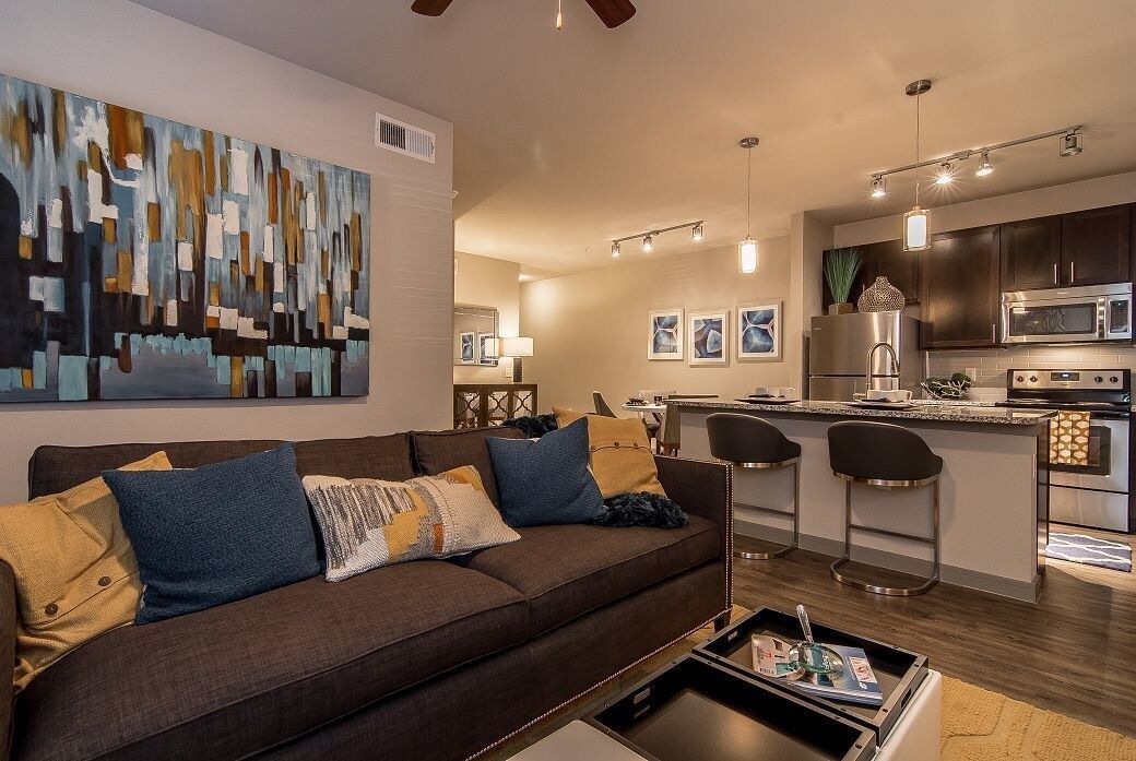 Living room with a brown sofa and colorful cushions, open kitchen with island and bar stools.