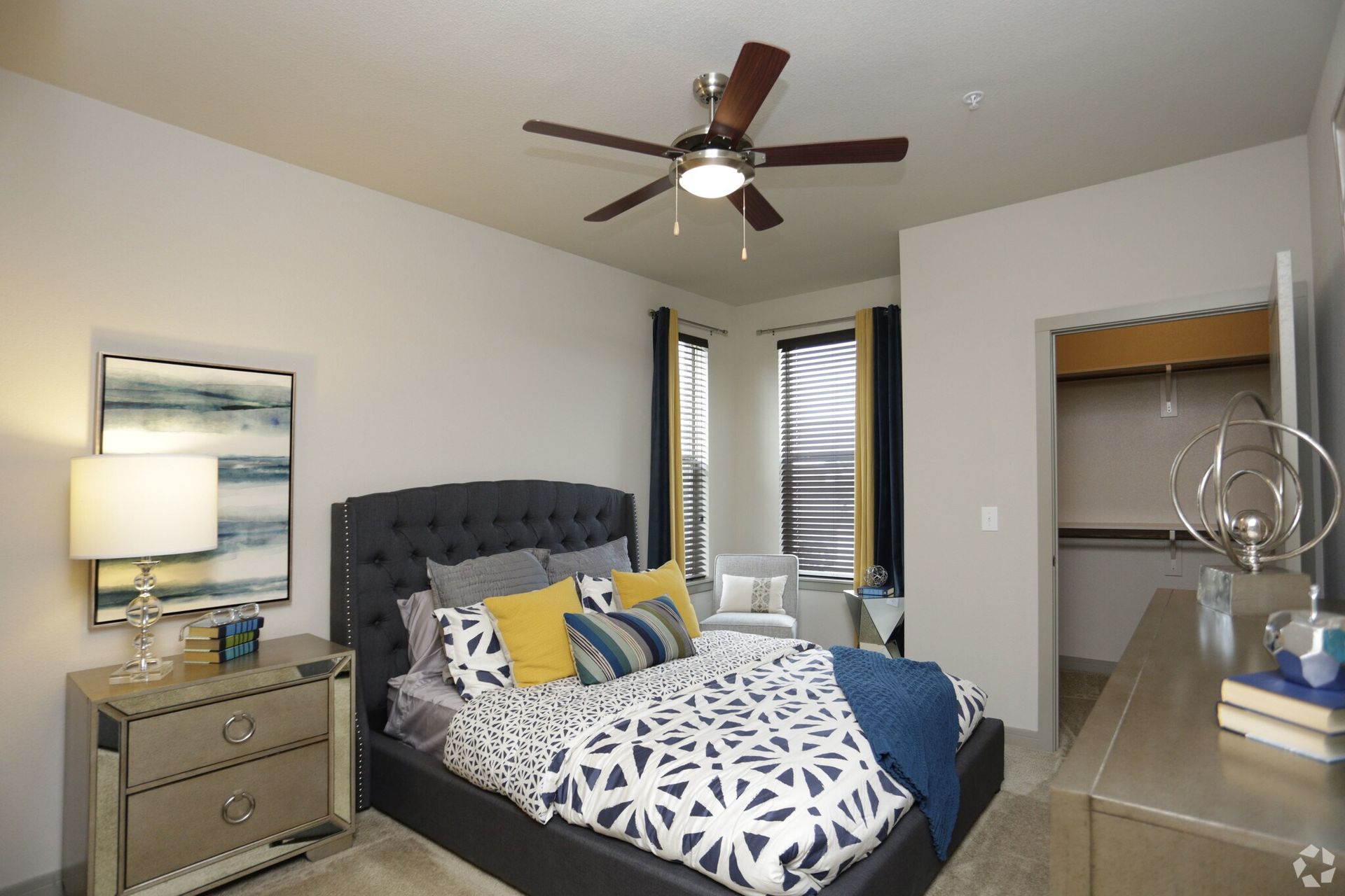 Bedroom featuring a gray upholstered bed, nightstand, lamp, ceiling fan, and open closet.