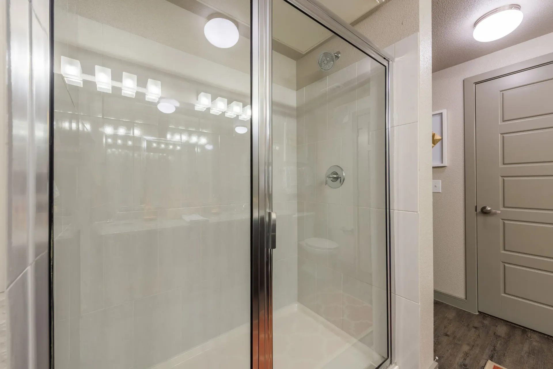 Glass shower enclosure with a chrome frame in a neutral apartment bathroom.