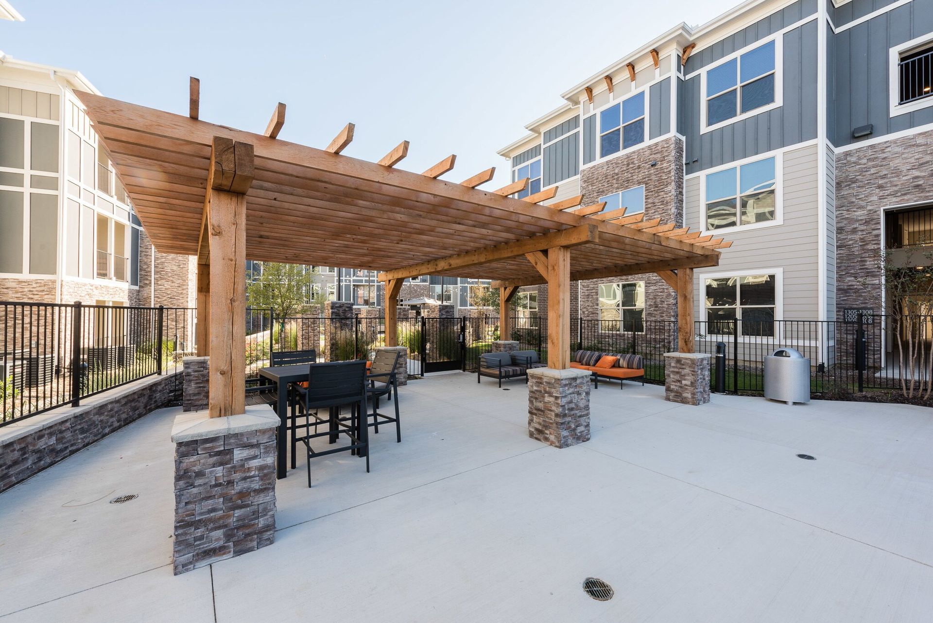 Outdoor communal seating under a wooden pergola in an apartment complex courtyard.