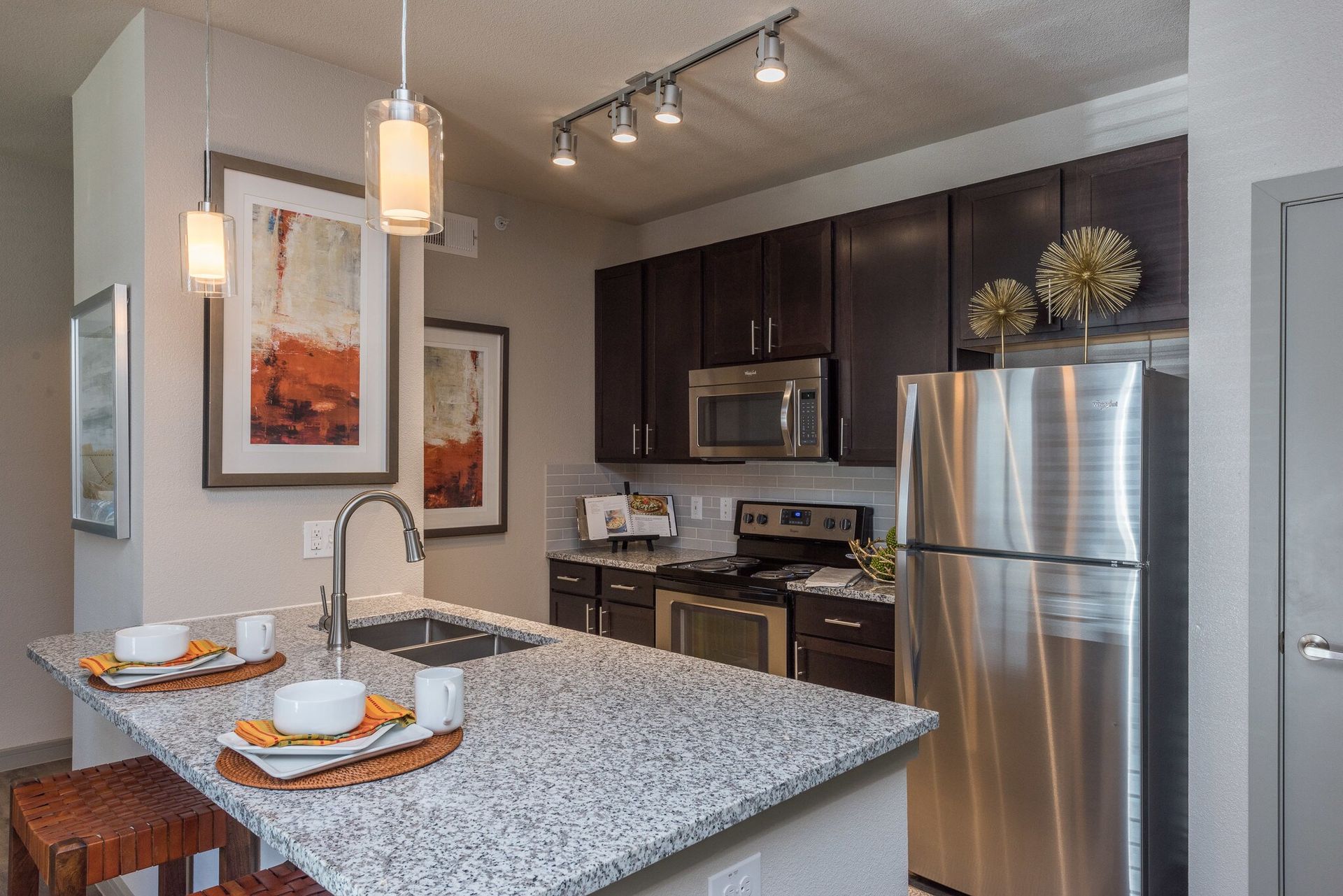 Modern apartment kitchen with granite island, stainless steel appliances, and dark wood cabinets.