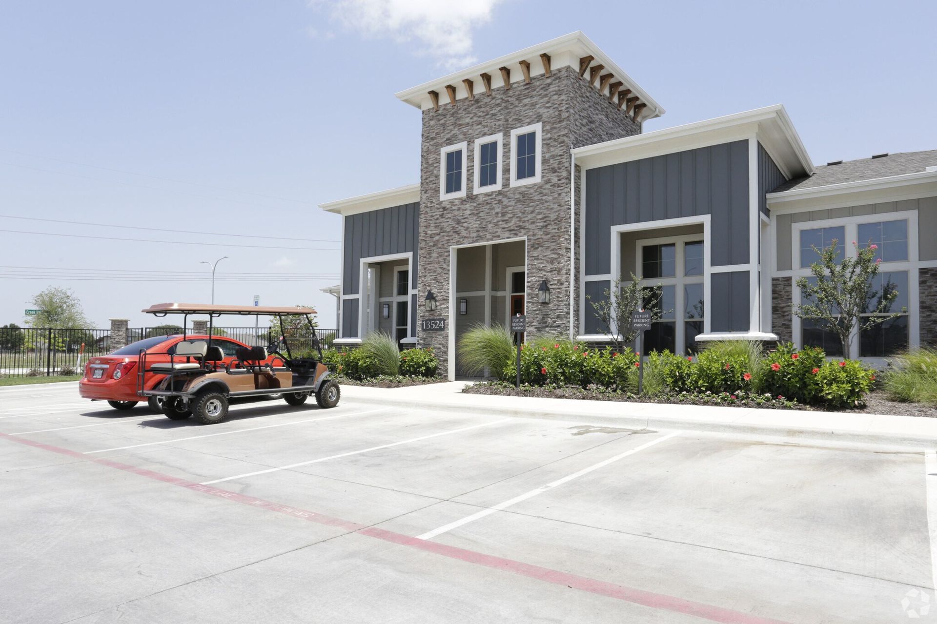 Exterior view of a multifamily leasing office with stone facade, landscaping, and a parked golf cart.