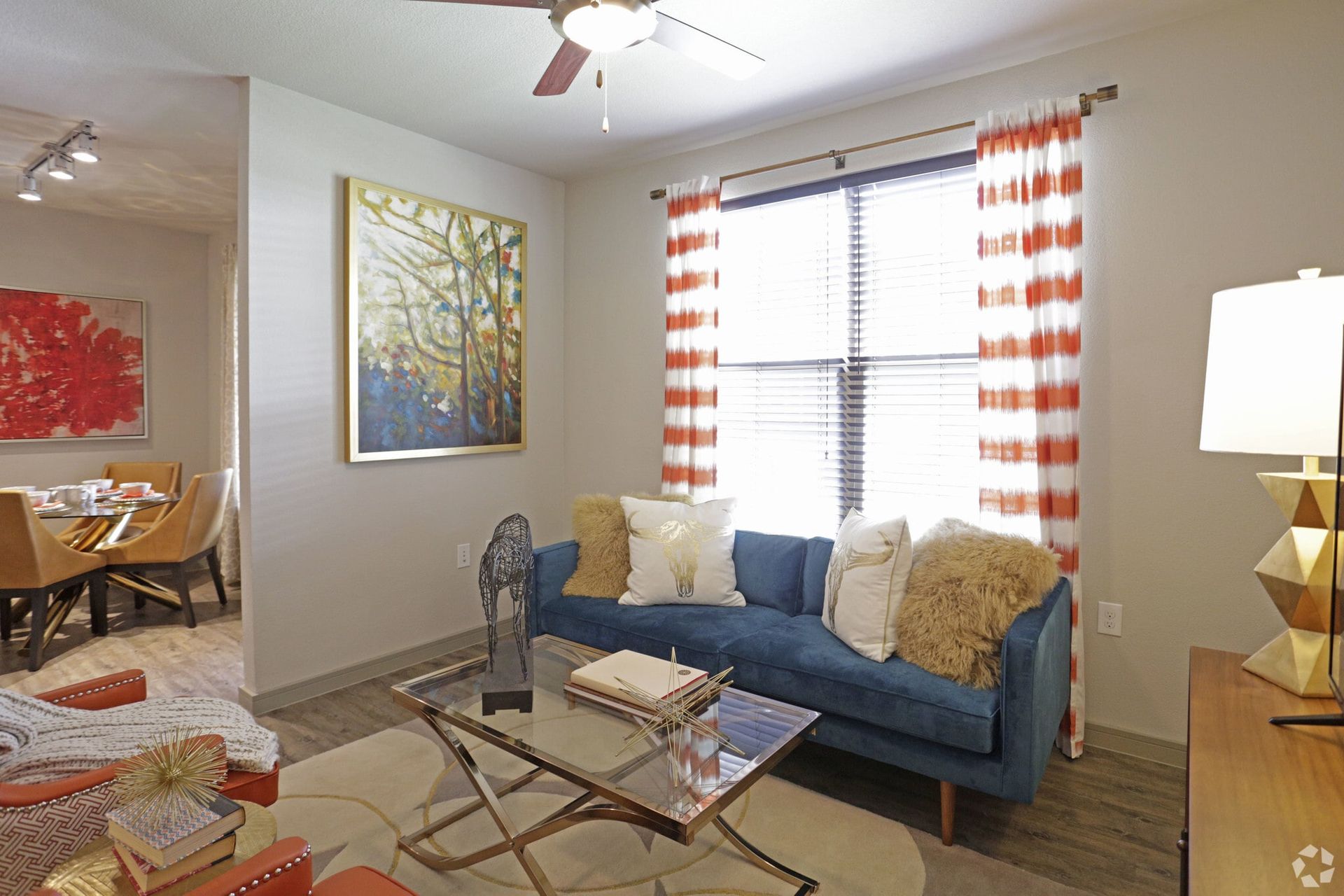 Living room with a blue sofa, glass coffee table, and orange-striped curtains.