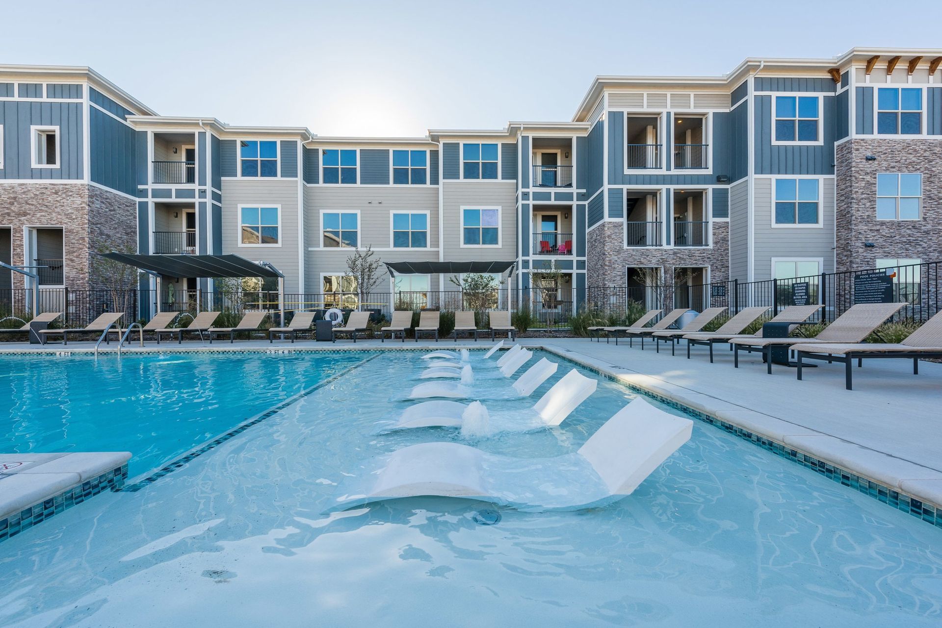 Outdoor community pool with loungers and a modern apartment building backdrop.