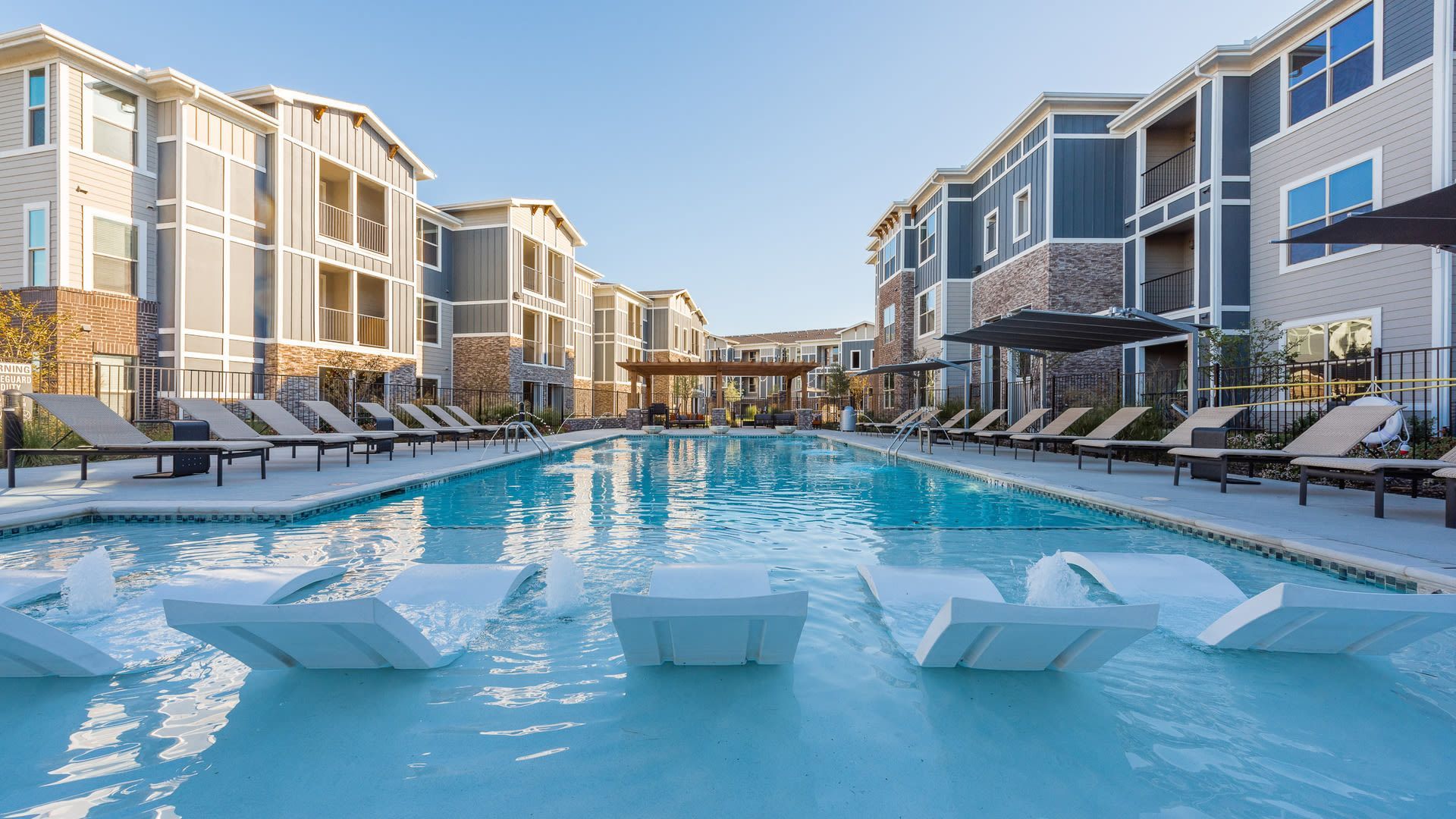 Outdoor apartment community pool with lounge chairs and surrounding buildings.