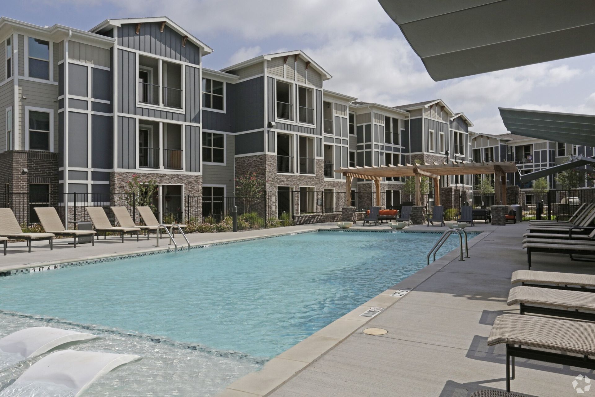 Outdoor pool area with lounge chairs and seating next to modern apartment buildings.