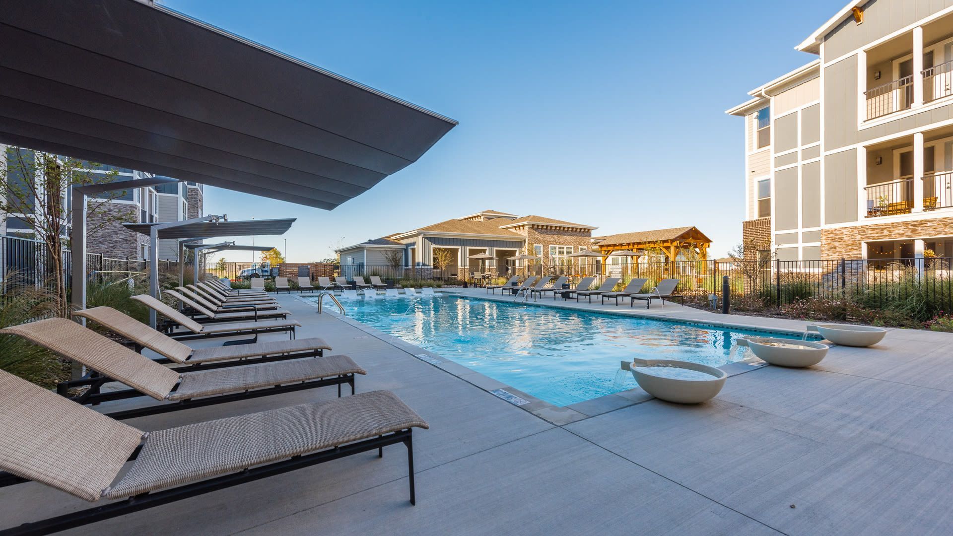 Outdoor community pool with lounge chairs and shade structures.