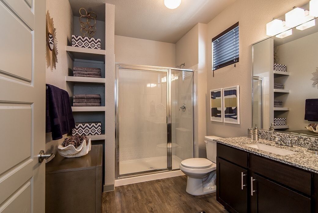 Bathroom in a modern apartment with a glass shower, toilet, and dark wood vanity with granite countertop.