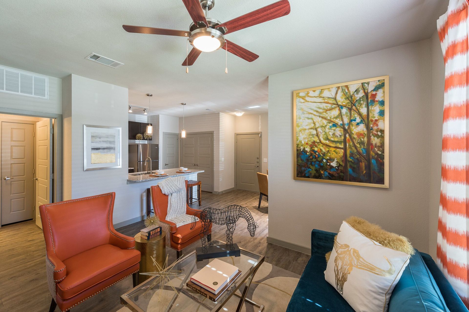 Open-concept living area with orange chairs, a teal sofa, and a kitchen island.