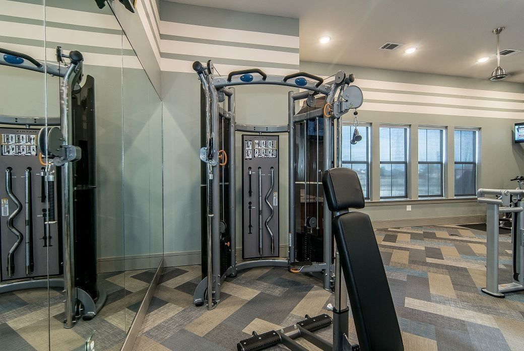 Modern apartment community gym with multi-station machines, bench, and mirrored walls.