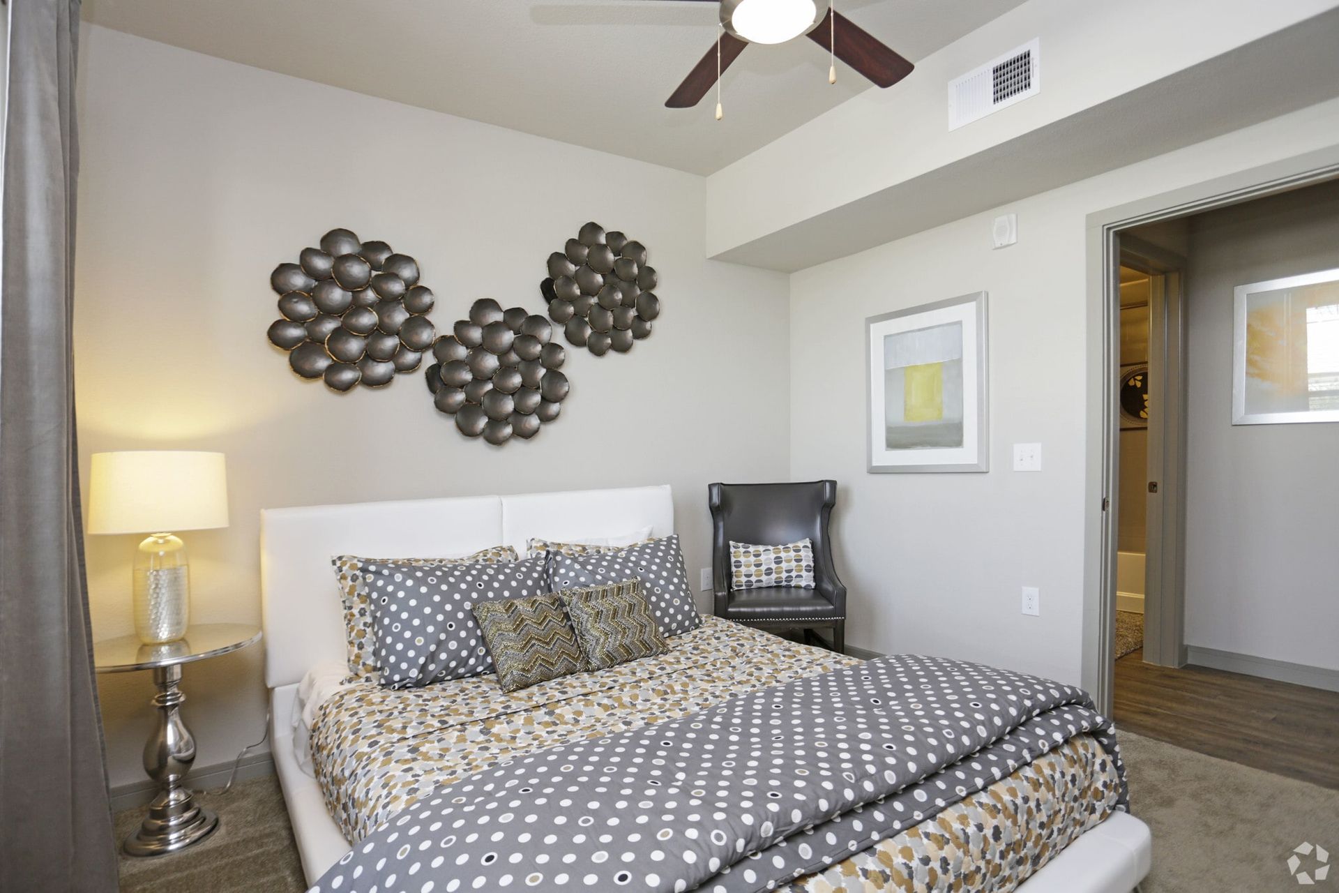 Bedroom in an apartment with a white upholstered bed, gray bedding, and a seating chair.