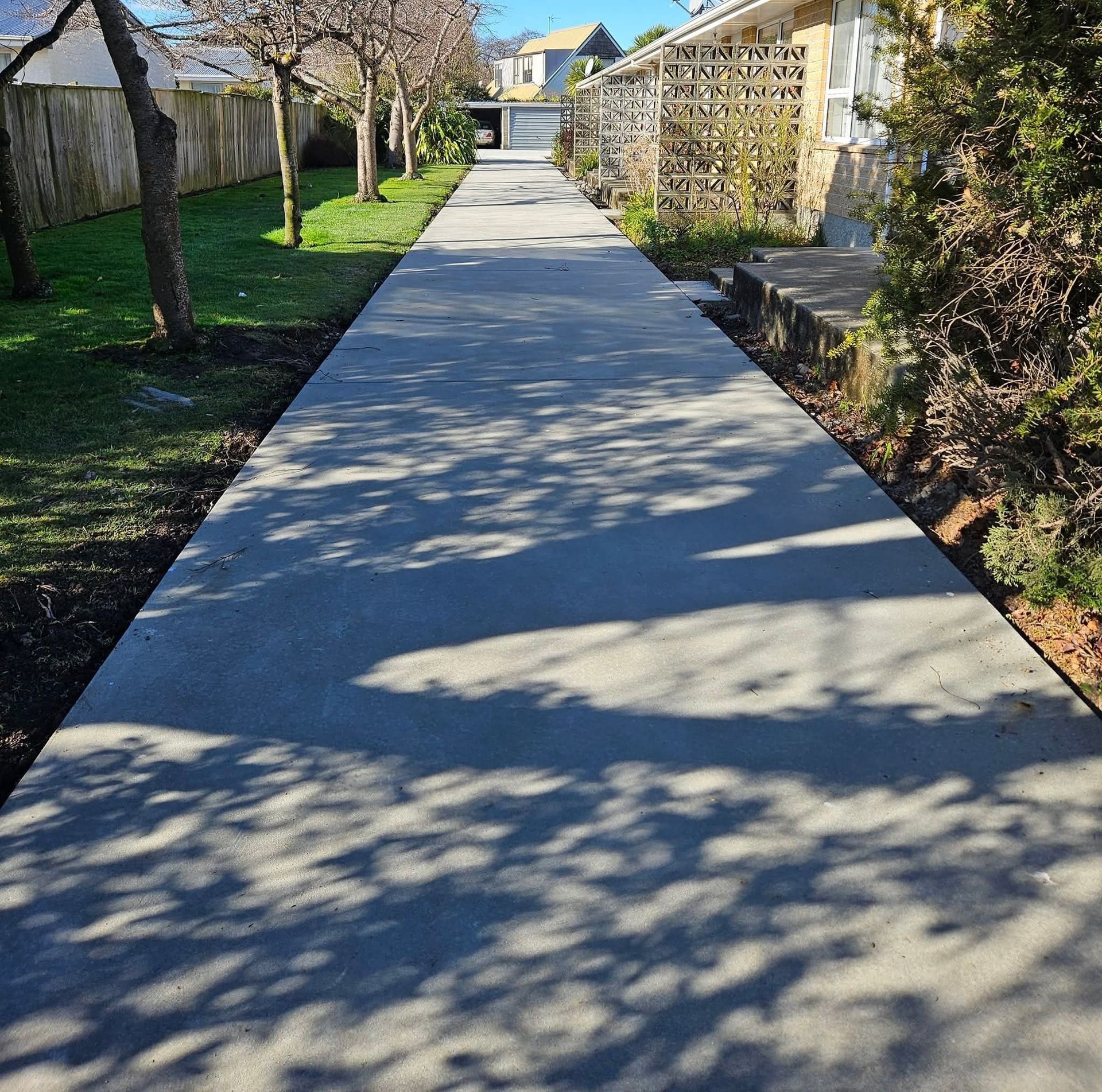 Dark driveway leading up to a gray house with a two-car garage, surrounded by landscaping and greenery.
