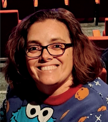 A woman wearing glasses and a cookie monster shirt smiles for the camera