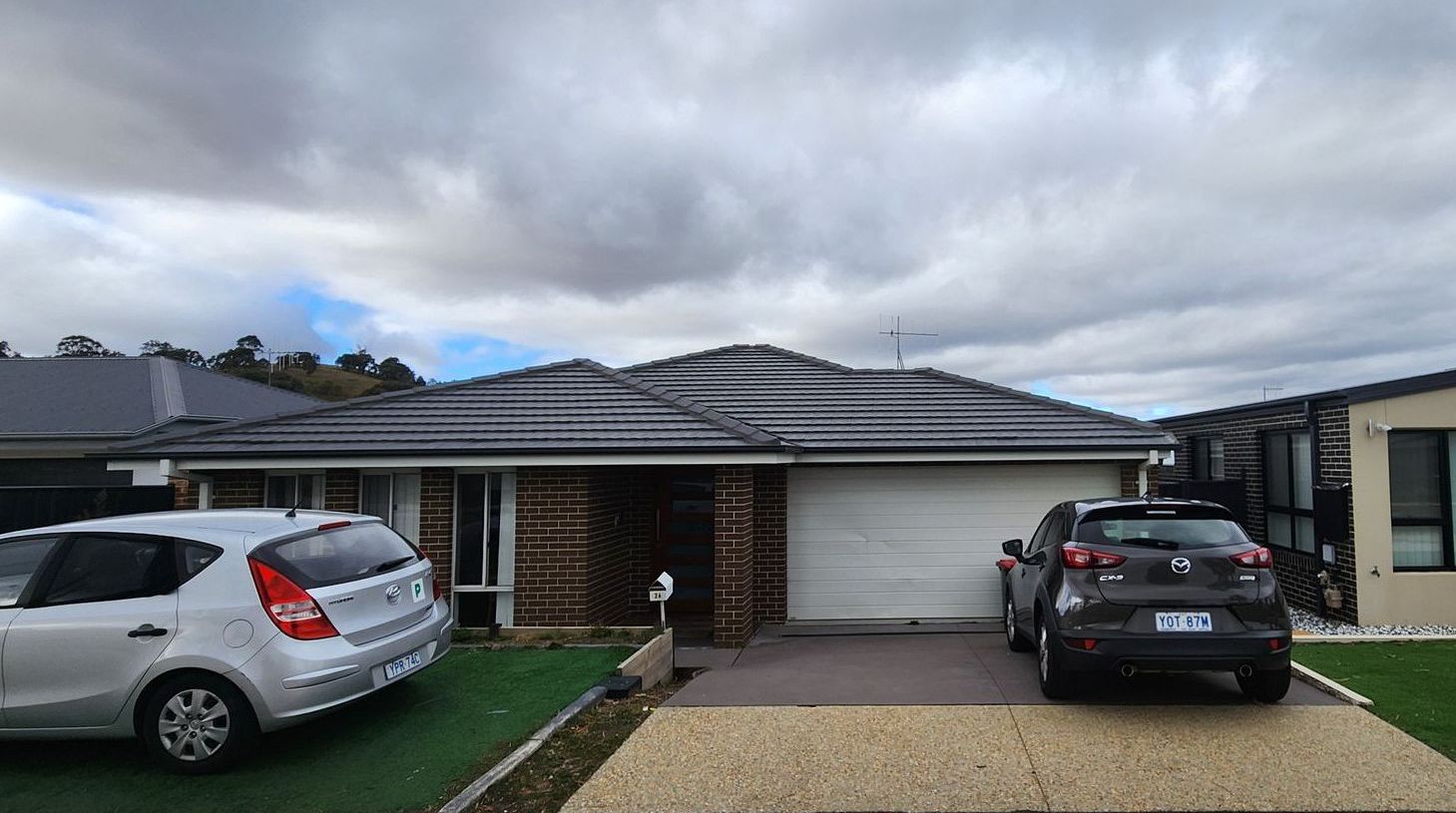 Two cars are parked in front of a house on a cloudy day.