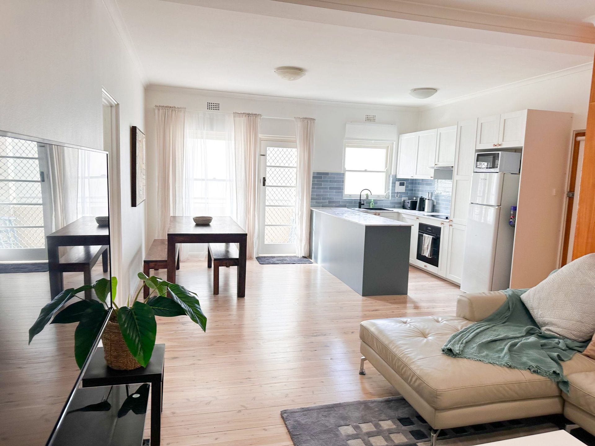 A living room with a couch , table and chairs and a kitchen in the background.