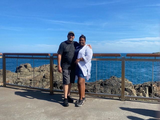 A man and a woman are posing for a picture in front of the ocean.