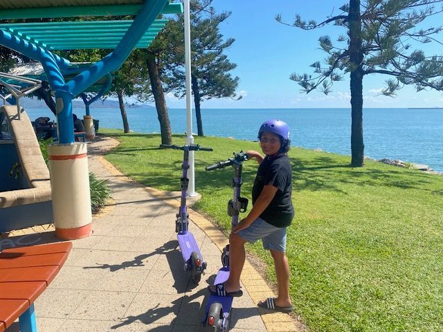 A young boy is riding a scooter on a sidewalk near the ocean.