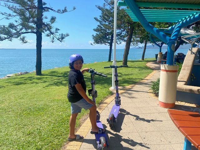 A young boy is riding a scooter on a sidewalk near the ocean
