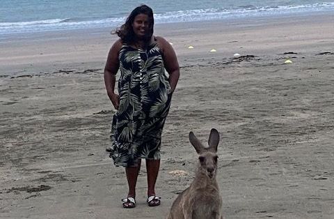 A woman is standing next to a kangaroo on the beach.