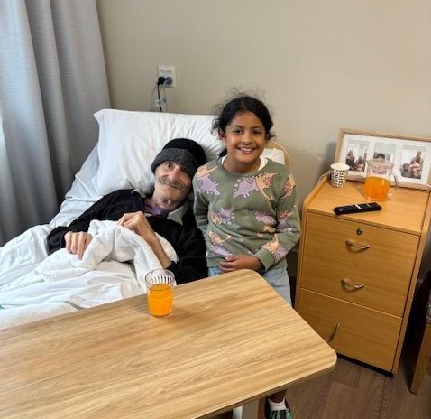A girl is sitting next to an older man in a hospital bed.