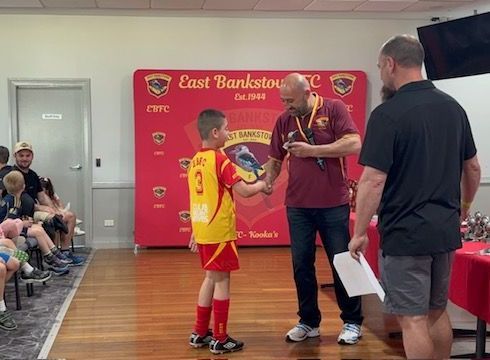 Two men are shaking hands with a young boy in a soccer uniform.