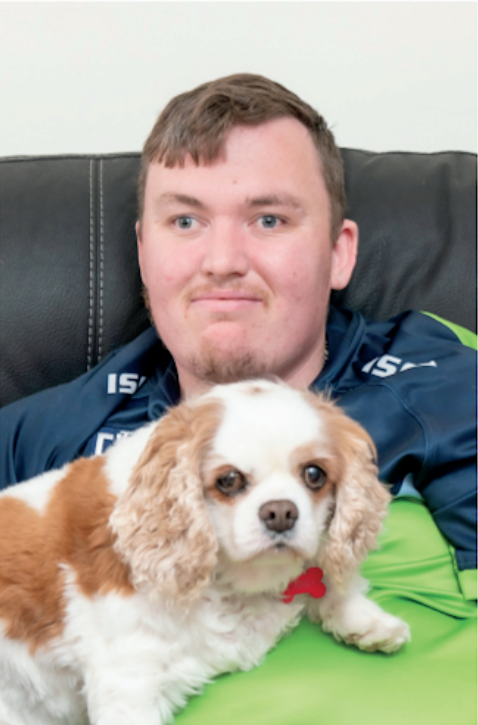 A man is laying on a couch holding a small brown and white dog