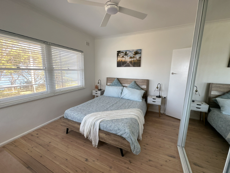 A bedroom with a bed , nightstands , a mirror and a ceiling fan.