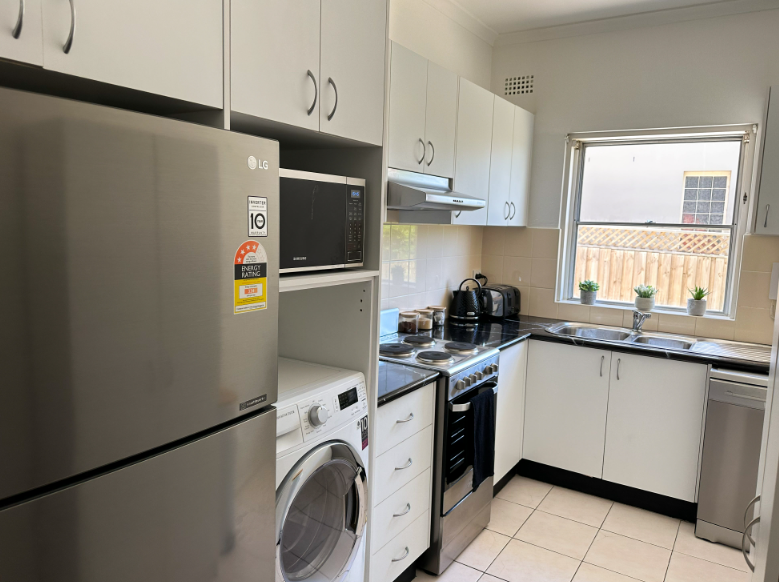 A kitchen with white cabinets , stainless steel appliances , a washer and dryer , and a refrigerator.