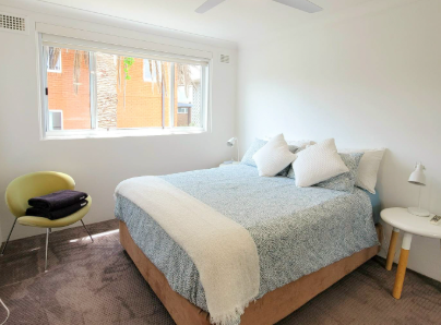 A bedroom with a bed , chair , table and window.
