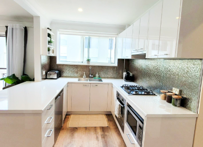 A kitchen with white cabinets , a stove , a sink , and a microwave.
