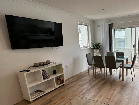A living room with a dining table and chairs and a flat screen tv on the wall.