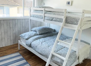 A bunk bed with a ladder in a bedroom next to a window.