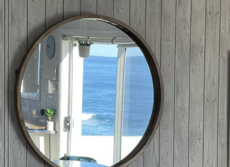 A round mirror on a wooden wall shows a view of the ocean