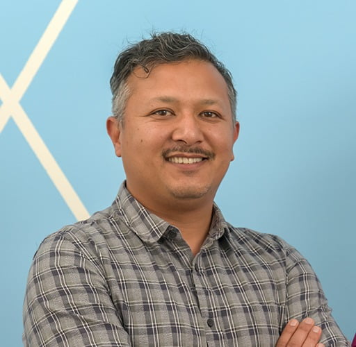 A man in a plaid shirt is standing with his arms crossed and smiling.