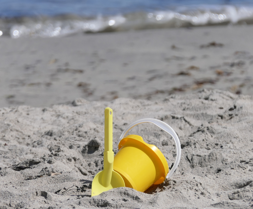 A yellow bucket and shovel are in the sand on the beach